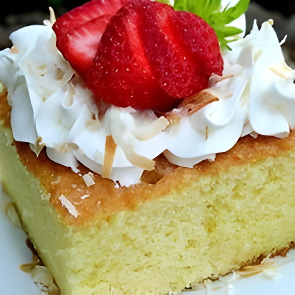 Slice of tres leches cake topped with whipped cream, strawberries, and toasted coconut flakes.