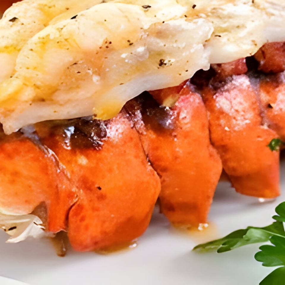 Close-up of grilled lobster tails with melted butter and a sprig of parsley.